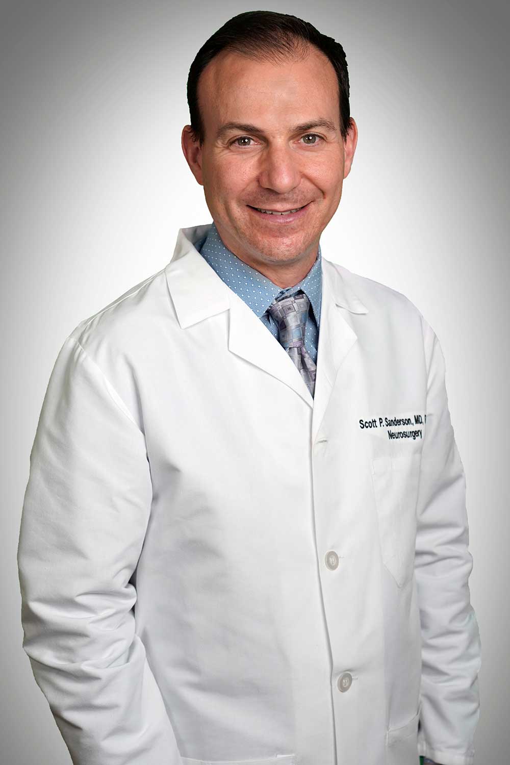 Headshot of chief neurosurgeon Scott Anderson wearing his lab coat and smiling.
