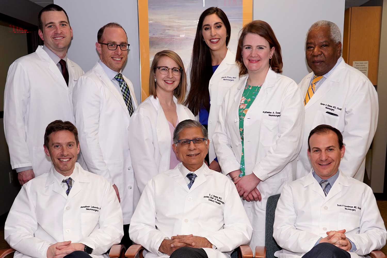 The neurosurgical specialists of Elite Brain & Spine of Connecticut taking a lively group photo in their lab coats.