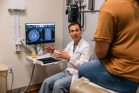 A doctor explain a scan of a spine to a patient in an exam room.