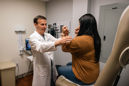 A male doctor examines a female patient's arm mobility.