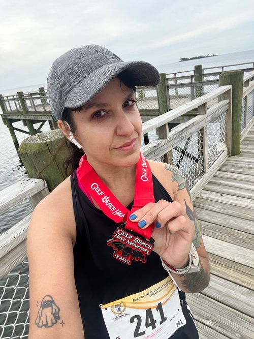 NH Spine Patient Carolina Herrera selfie with her half marathon medal standing on a boardwalk